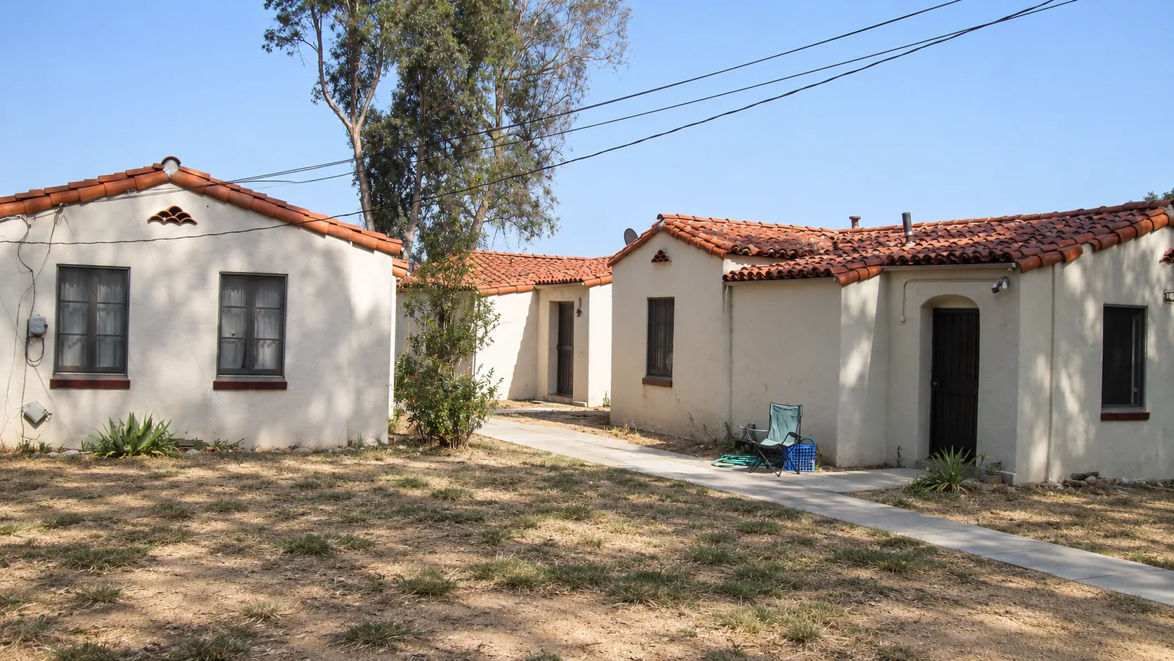 Concept image: Spanish-style stucco homes with clay tile roofs around a dry lawn.