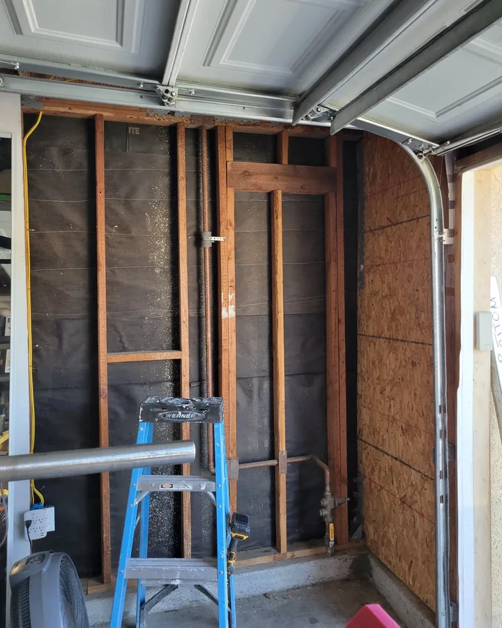 Site photo: wood framing and sheathing inside a garage, with a ladder and the overhead door track above.