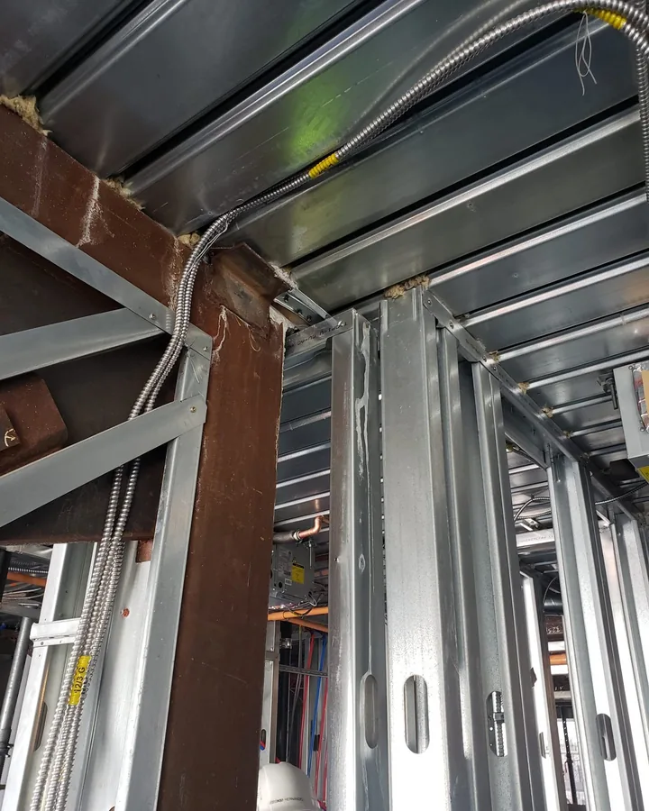 Site photo: a steel beam, metal studs and conduit inside a building under construction.