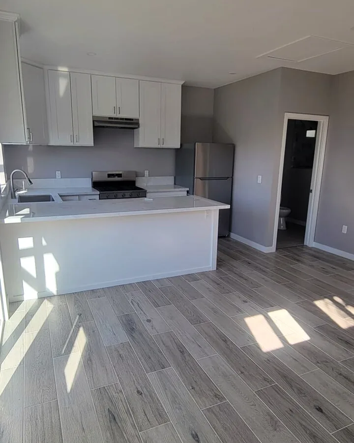 Site photo: a finished kitchen with white cabinets, an island and wood-look floors.