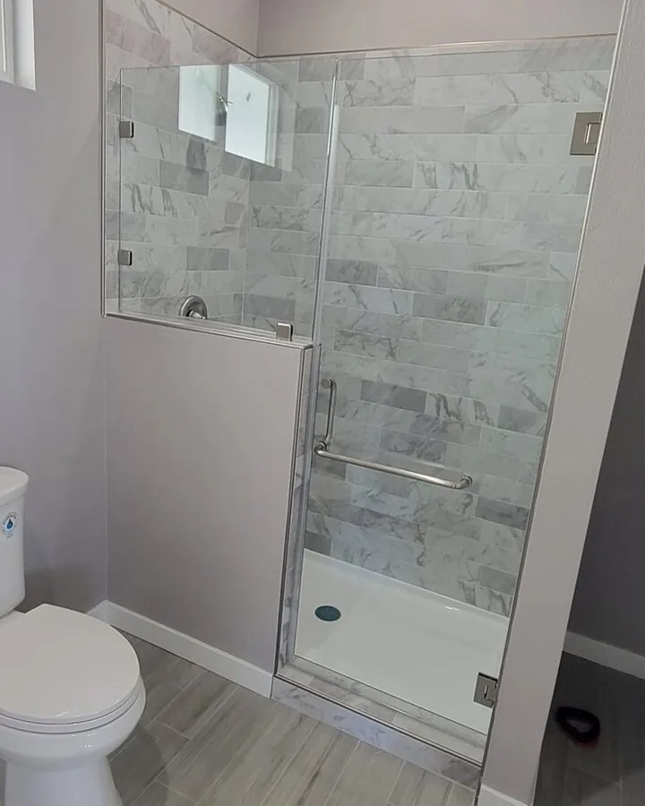 Site photo: a finished bathroom with a glass shower, marble-look tile and a toilet.