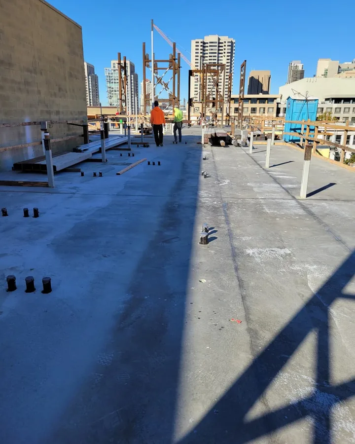 Site photo: a rooftop deck with steel posts and two workers, with downtown towers behind.