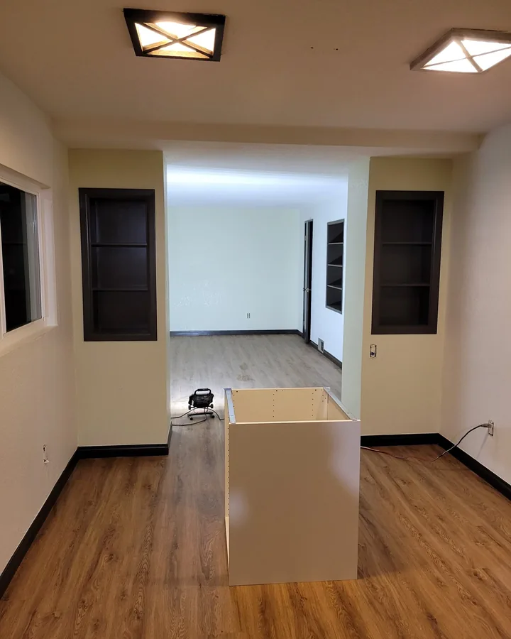 Site photo: a room with dark built-in shelves on both sides of an opening and wood floors.