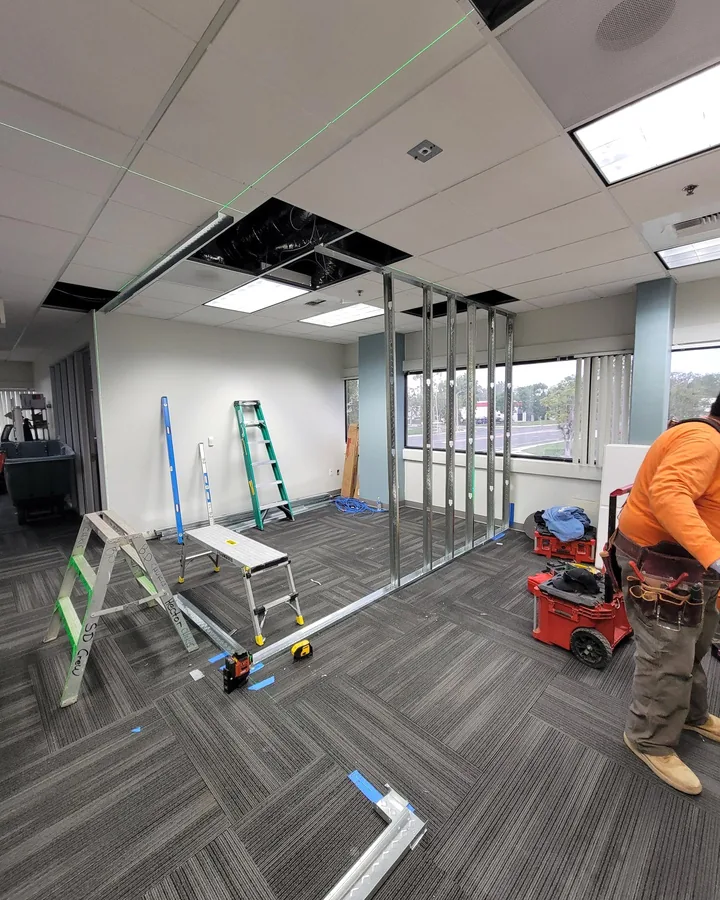 Site photo: an office tenant improvement in progress, with metal stud partitions, carpet tile and a worker.