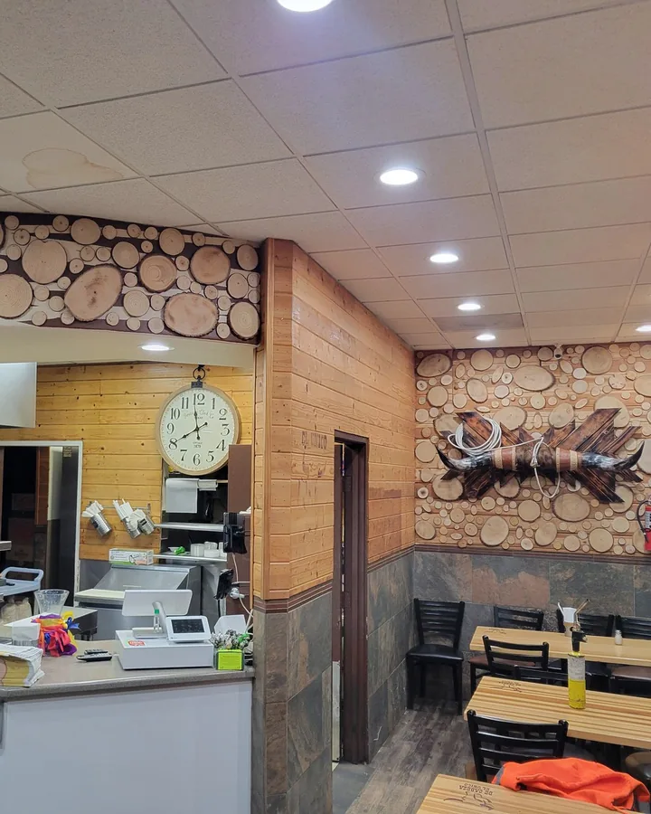 Site photo: a small restaurant with pine walls, a wood-slice feature wall, a clock and tables.