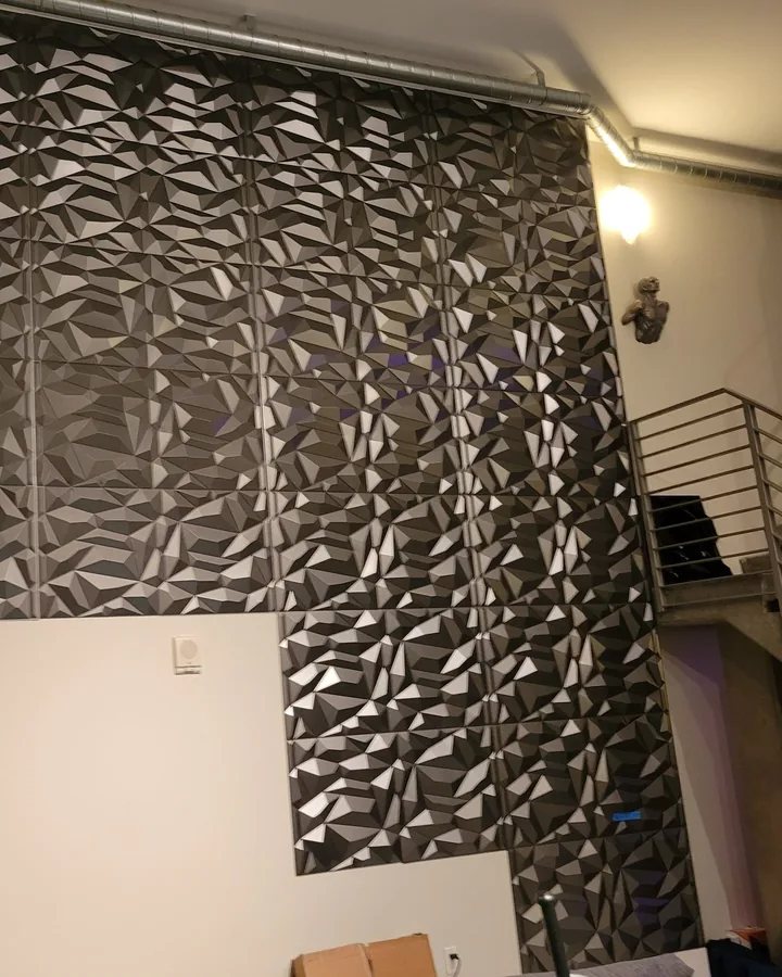 Site photo: a double-height wall covered in dark 3D panels, next to a metal stair.